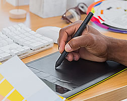 A hand using a stylus on a computer graphics tablet beside colour swatches.